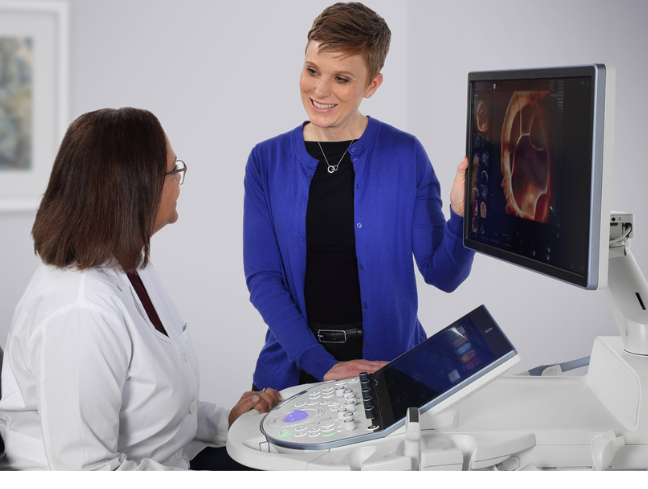 Eine Ärztin und eine Geschäftsfrau stehen neben einem Ultraschallgerät und unterhalten sich