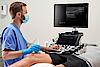 Na zdjęciu widać lekarza przeprowadzającego badanie ultrasonograficzne MSK kolana pacjenta.
