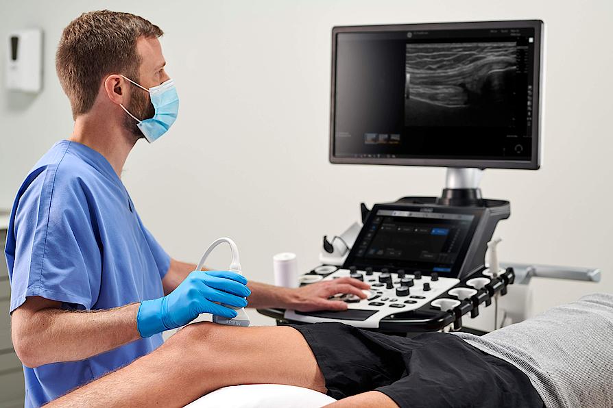Η εικόνα δείχνει έναν ιατρό που εκτελεί μυοσκελετική υπερηχογραφική εξέταση στο γόνατο ενός ασθενούς.