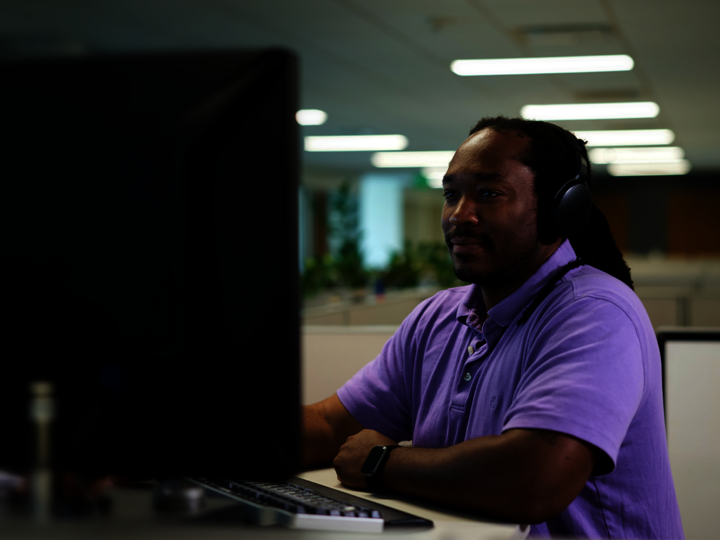 Ein Mann mit Headset sitzt an seinem Büroschreibtisch und arbeitet am PC
