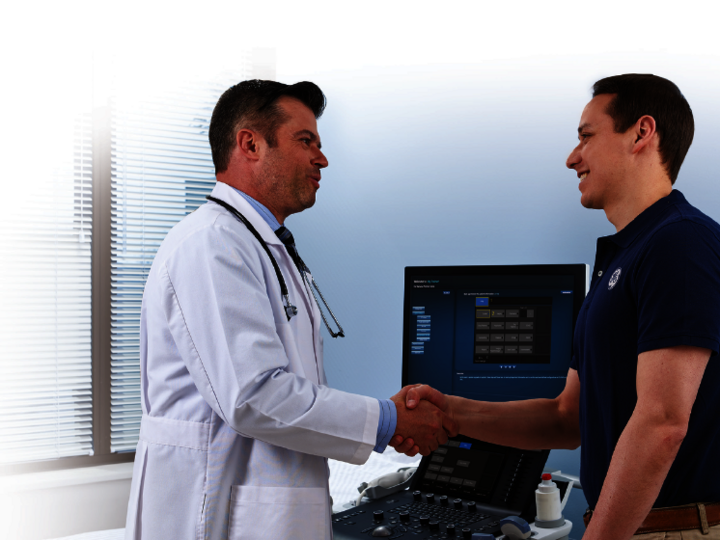 A doctor and a technician shaking hands in front of an ultrasound system