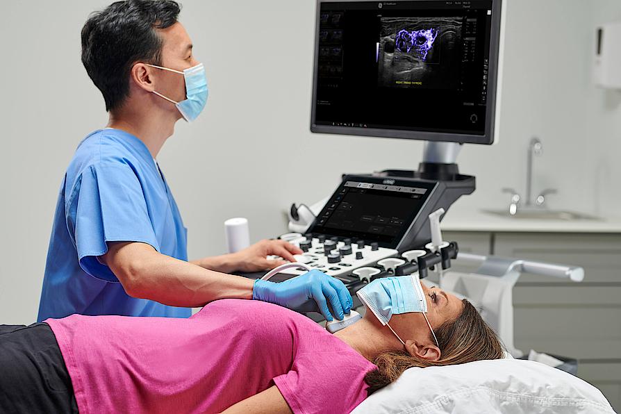 Imaginea prezintă un medic care efectuează o ecografie tiroidiană unui pacient.