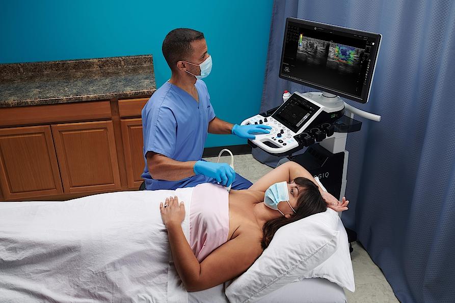Das Bild zeigt einen Arzt, der eine Ultraschalluntersuchung bei einer weiblichen Brust durchführt.