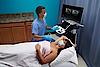 Das Bild zeigt einen Arzt, der eine Ultraschalluntersuchung bei einer weiblichen Brust durchführt.