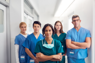 A group of doctors is standing with folded arms in the aisle of a hospital.