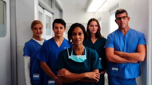 A group of doctors is standing with folded arms in the aisle of a hospital