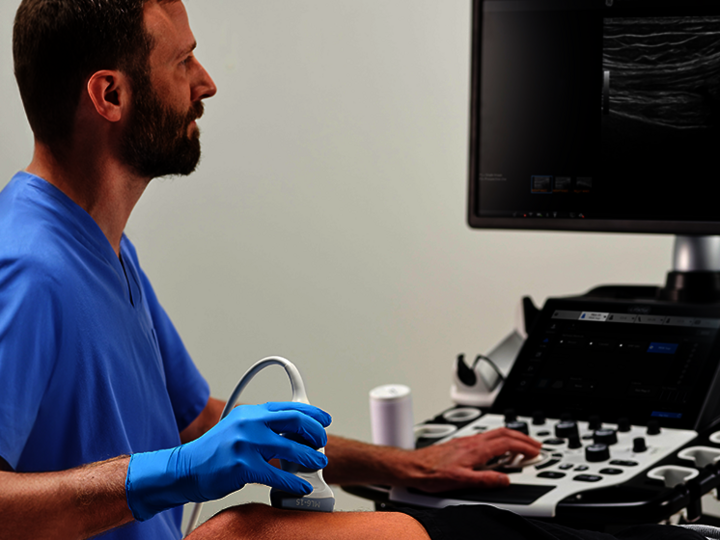 Ein Arzt führt eine MSK-Ultraschalluntersuchung am Knie eines Patienten durch