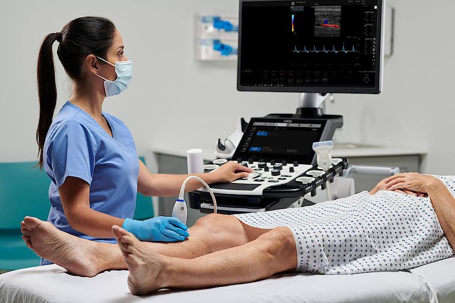 Η εικόνα δείχνει έναν ιατρό που εκτελεί αγγειακή υπερηχογραφική εξέταση σε έναν ασθενή.