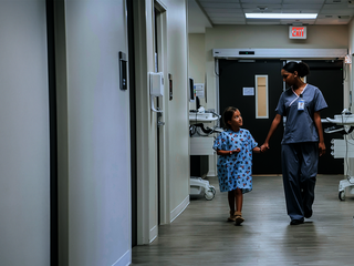 Eine Ärztin führt ein Mädchen an der Hand durch einen Krankenhausflur