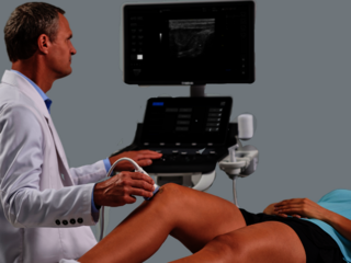 A doctor performing an MSK ultrasound exam on a patient's knee