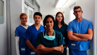 A group of doctors is standing with folded arms in the aisle of a hospital.