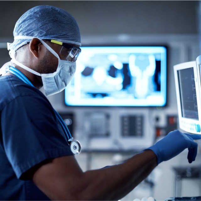 Ein Arzt in OP-Kleidung steht in einem OP und arbeitet an einem Ultraschallgerät